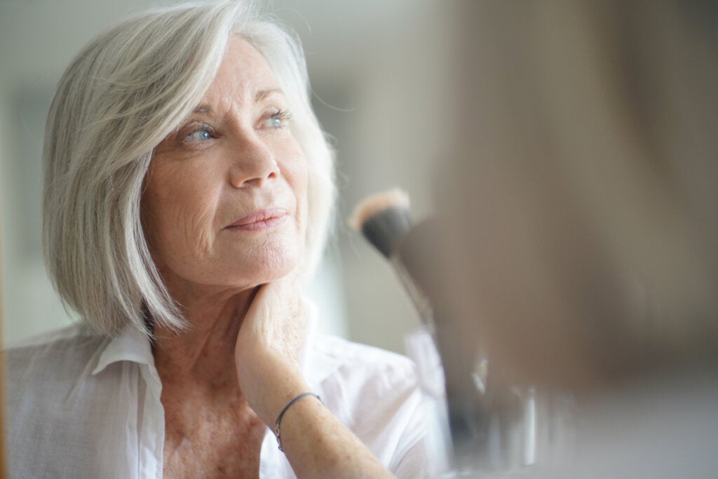 Yaşlı kadın aynaya bakıyor ve beyin yaşlanmasını nasıl tersine çevireceğini düşünüyor.